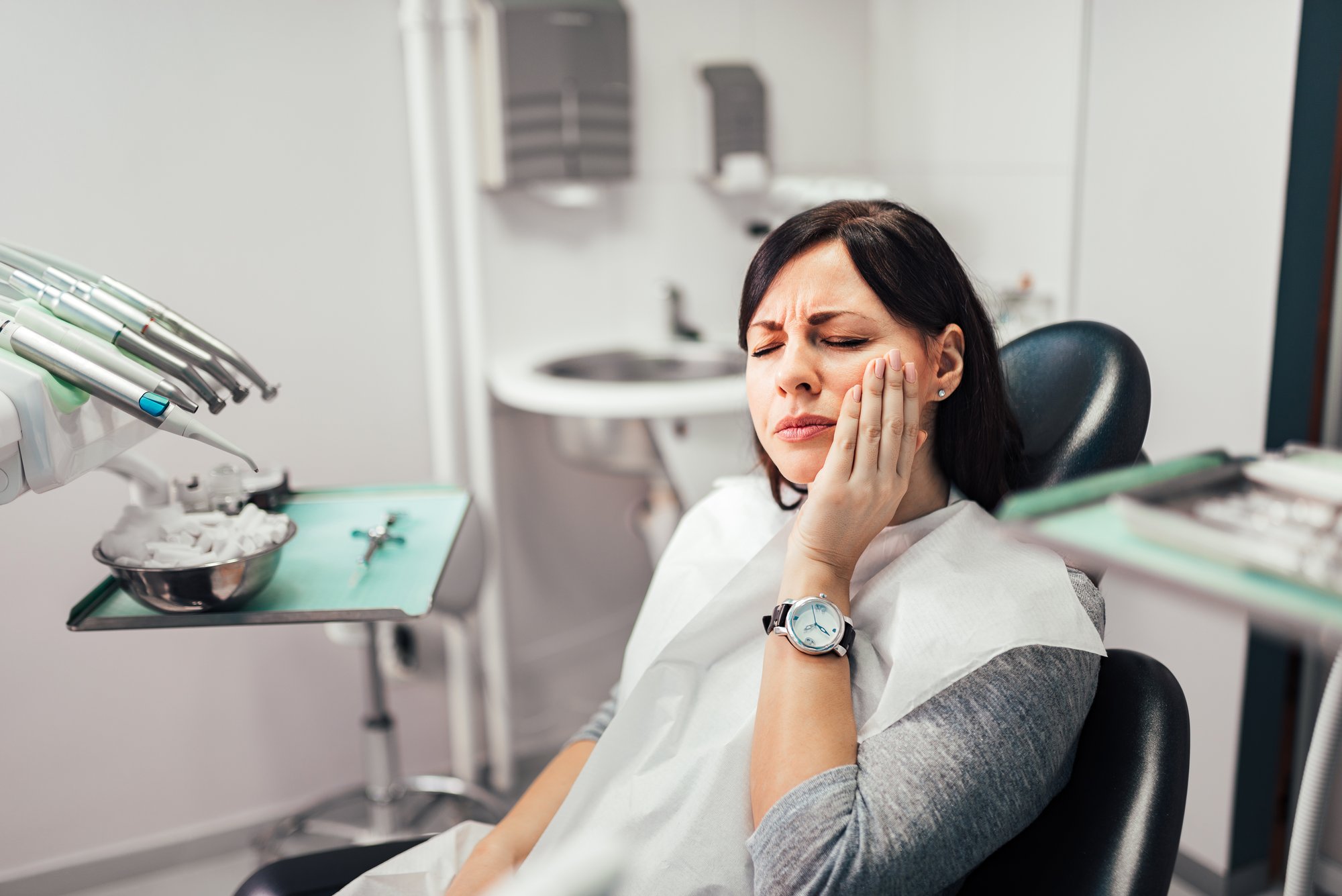 A patient calling an emergency dentist while holding their cheek in pain